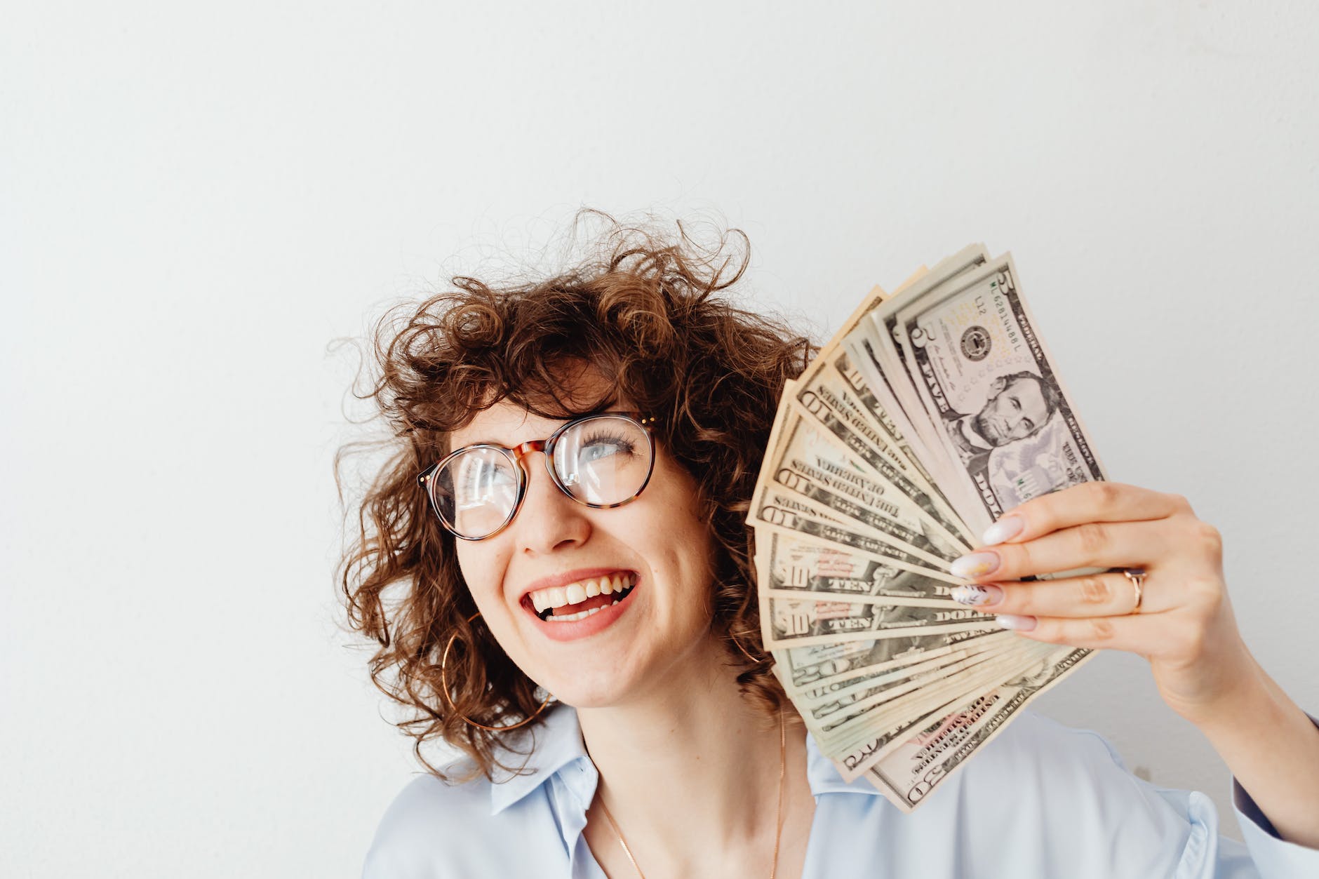 a woman holding us dollar bills and looking happy representing money and happiness.
