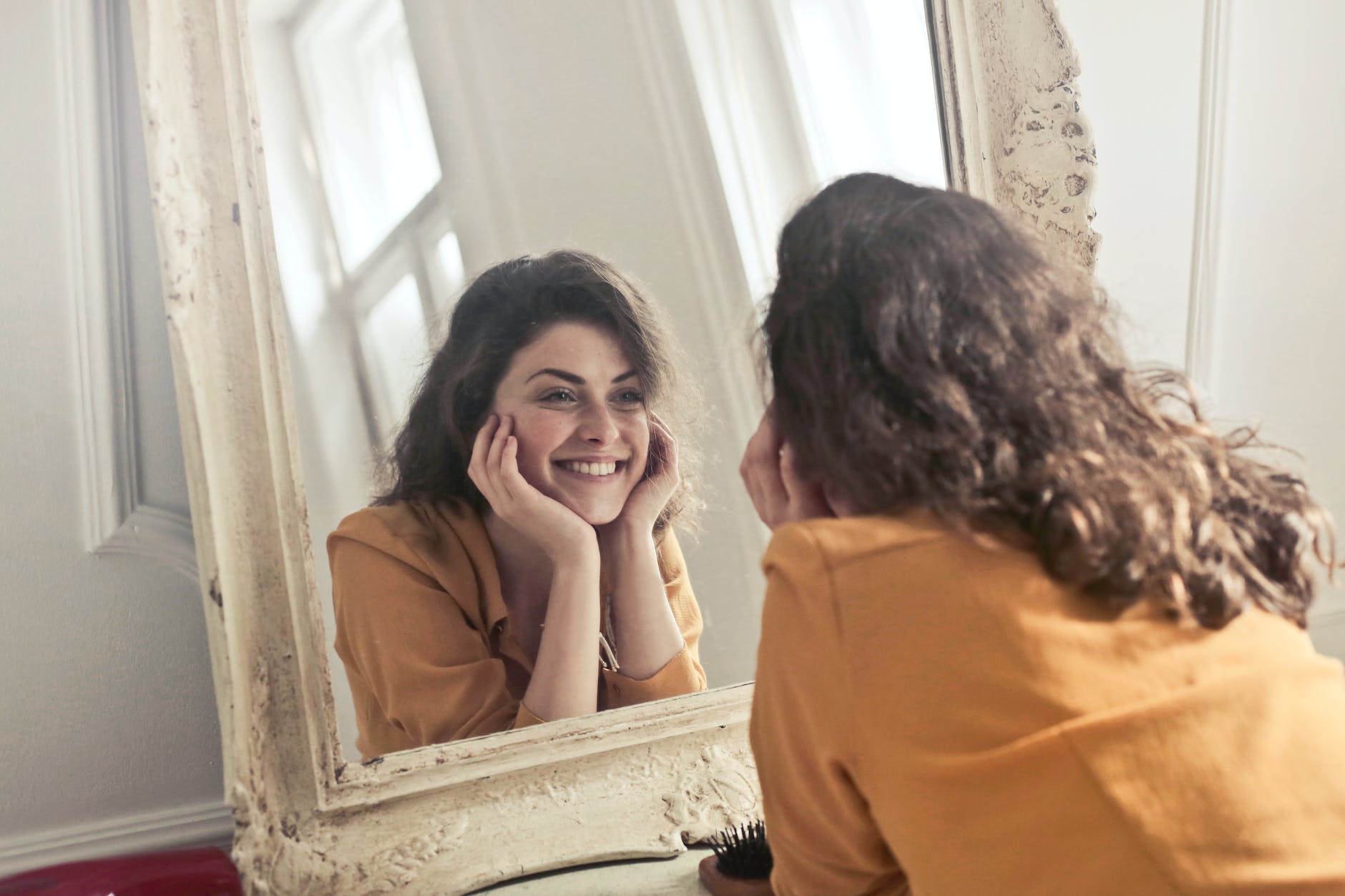 A person standing in front of the mirror and smiling symbolizing the empowerment achieved through positive self-talk.