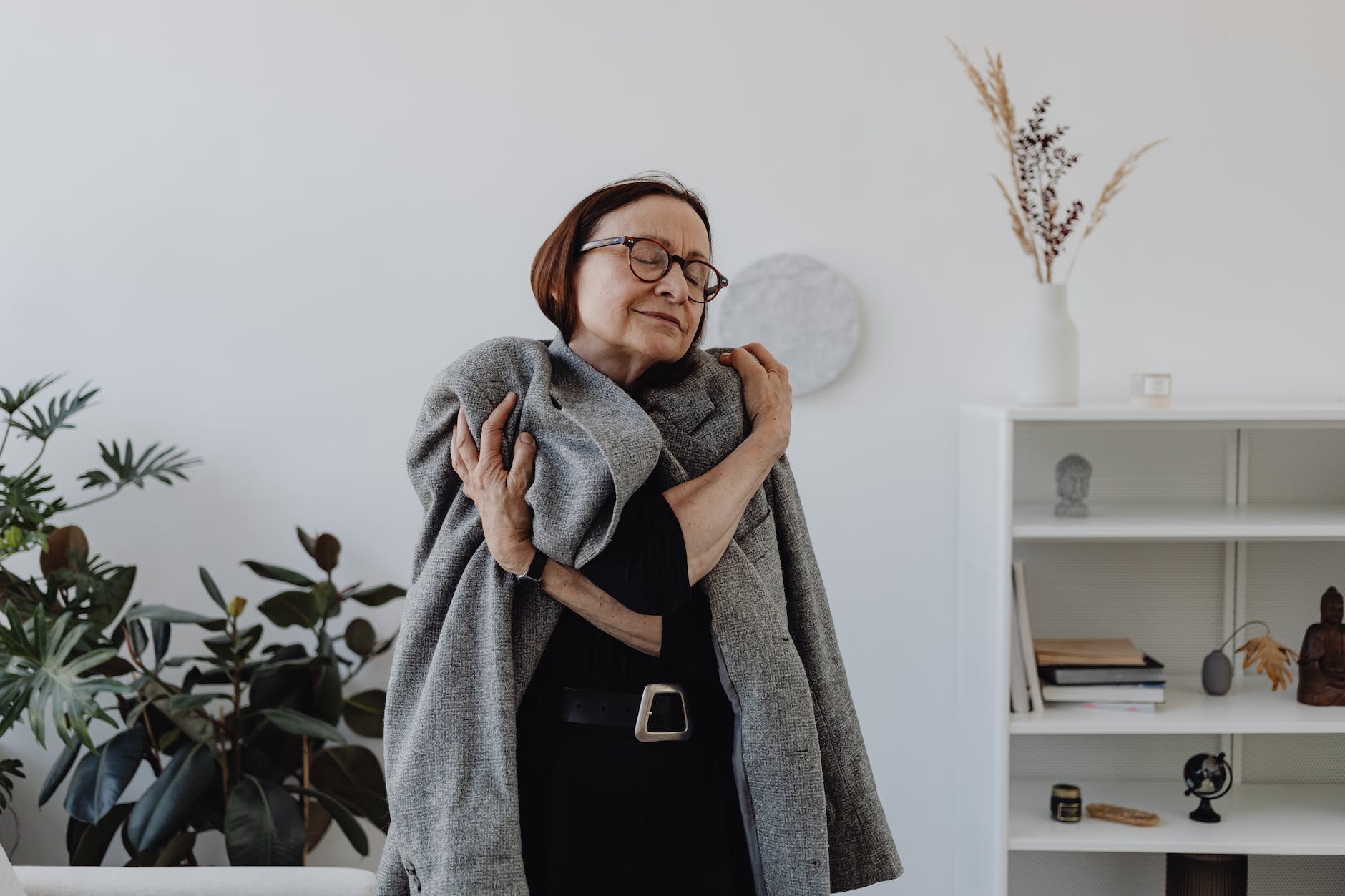 an elderly woman in gray coat embracing herself