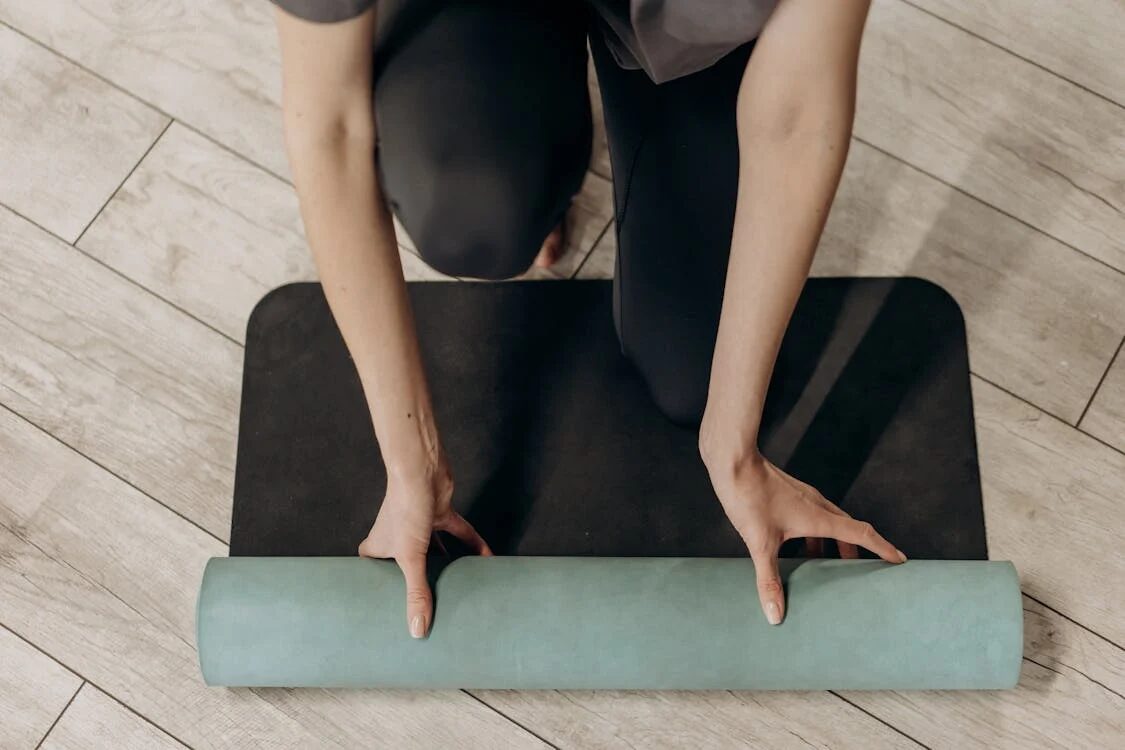 A woman unrolling a yoga mat on a clean, well-lit floor. This image symbolizes the preparation and intention behind establishing habits, routines, and systems.