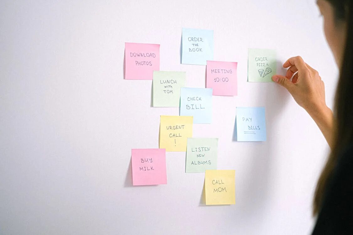 Woman adding sticky notes with to-do list items on a white wall, illustrating task prioritization and the Eisenhower Matrix concept